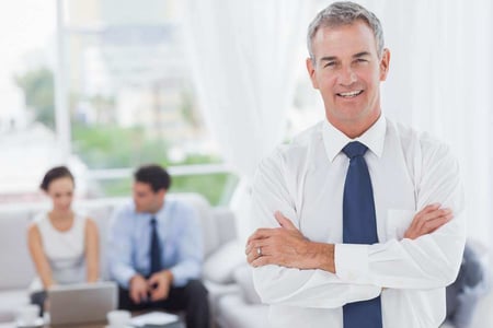 Executive posing while his colleagues are working in cosy meeting room Executive posing while his colleagues are working in cosy meeting room